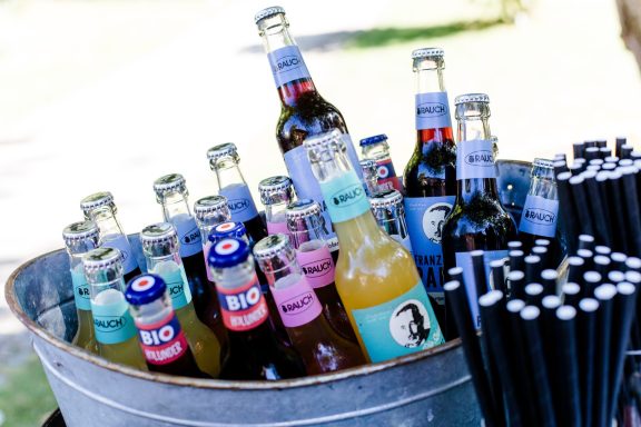 Bunte Flasche in einem Eimer, umgeben von schwarzen Strohhalmen.