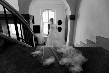 Braut in einem weißen Kleid steht auf einer Treppe, umgeben von fließendem Stoff.