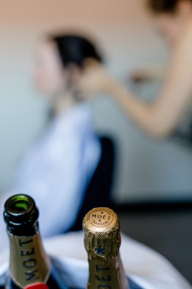 Schnapsflaschen im Vordergrund mit einer Person, die Haare frisiert, im Hintergrund.