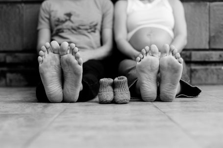 Zwei Erwachsene mit nackten Füßen sitzen neben einem Paar kleiner Babyfüße.
