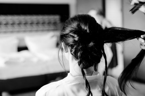 Frau mit langen, dunklen Haaren, die frisiert wird, im Hintergrund ein Zimmer.