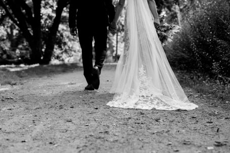 Hochzeitskleid und Herrenschuh auf einem Waldweg, umgeben von Bäumen.