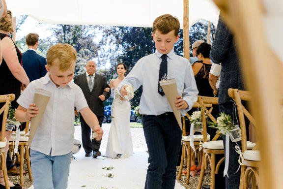 Zwei Jungen streuen Blütenblätter auf dem Boden, während die Braut einläuft.