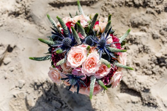 Bunten Blumenstrauß mit Rosen und Schleierkraut auf sandigem Untergrund.