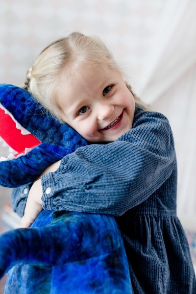 Ein Mädchen in einem blauen Kleid umarmt ein großes, blaues Stofftier.