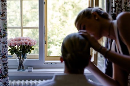Frisör schneidet Haare einer Person vor einem Fenster mit Blumen im Hintergrund.