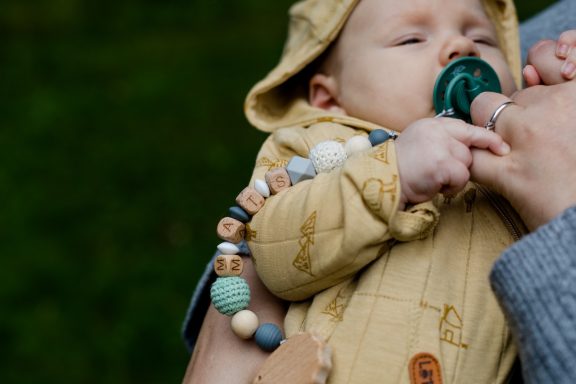 Baby mit Schnuller, in einer gelben Jacke, wird von einer Person gehalten.
