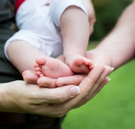 Hände halten die Füße eines Babys im Freien.