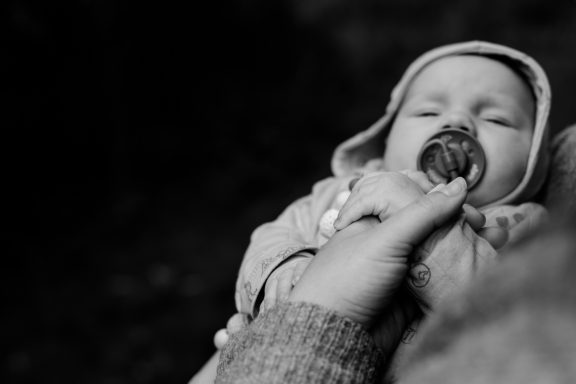 Ein Baby mit Schnuller wird sanft von einer Hand gehalten.
