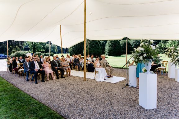 Hochzeitszeremonie im Freien unter einem Zelt mit Gästen in eleganter Kleidung.