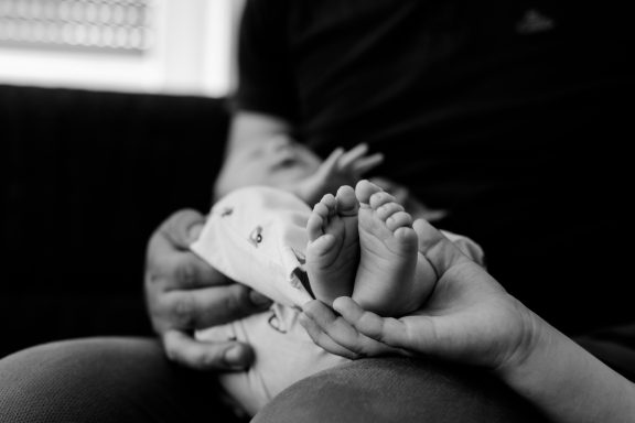 Hände halten die Füße eines Babys, sanfte, liebevolle Berührung.