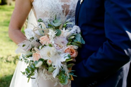 Brautpaar hält einen Brautstrauß mit weißen und orangenen Blumen.