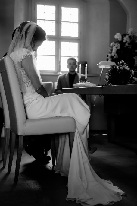 Hochzeitsbraut in einem eleganten Kleid, sitzt an einem Tisch und betrachtet den Boden.
