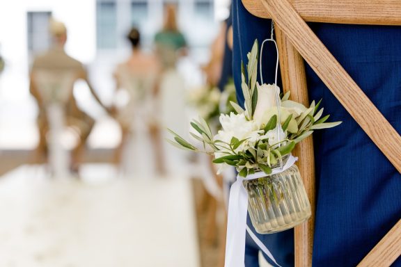Ein dekorierter Stuhl mit einer kleinen Blumenvase und weißen Blumen bei einer Hochzeit.