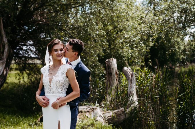 Hochzeitspaar im Freien, umarmt vor einer grünen Kulisse.