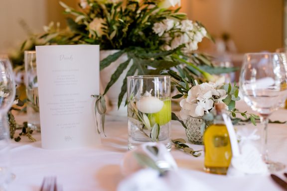 Eleganter Tisch gedeckt mit einer Speisekarte, Blumenarrangements und dekorativen Gläsern.