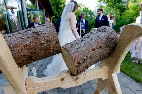 Hochzeitszeremonie im Freien mit Baumstämmen im Vordergrund. Braut und Bräutigam sichtbar.