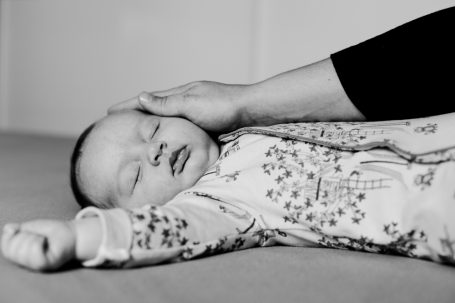 Ein schlafendes Baby wird sanft von einer Hand gestreichelt.