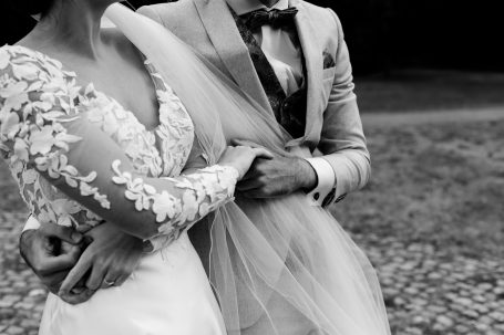 Brautpaar in eleganter Hochzeitskleidung, Arm in Arm, umgeben von Natur.