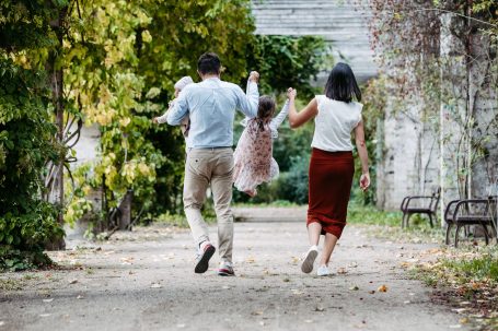 Familie geht Hand in Hand in einem Park, während sie ein Kind fröhlich schwingen.