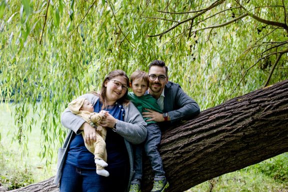 Familie posiert im Freien unter einem Baum, hält ein Kaninchen und umarmt sich.