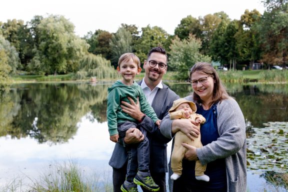 Familie steht am Ufer eines Sees mit einem Kind und einem Baby in den Armen.