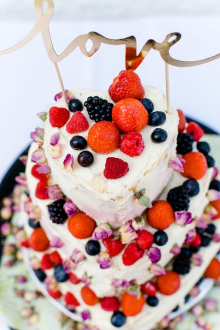 Dreistöckige Torte mit Beeren, Blüten und einer "Love"-Dekoration oben.