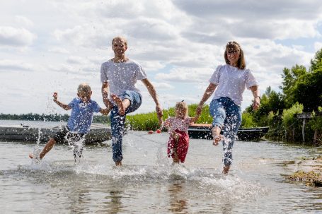 Familie spielt im Wasser, spritzt mit den Füßen; fröhliche Kinder und Erwachsene.