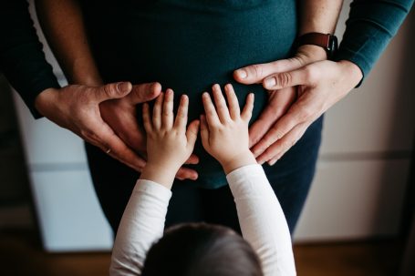 Hände berühren einen Babybauch, während ein Kind die Hände darauf legt.