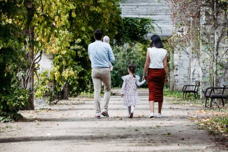 Familie spaziert auf einem Weg durch einen parkähnlichen Garten.