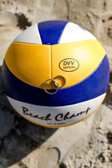 Voller Beachvolleyball mit blau-gelben Streifen auf sandigem Untergrund.