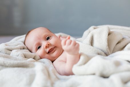 Lächelndes Baby liegt auf einer Decke, umgeben von einem weichen, hellen Stoff.