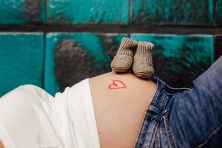 Schwangere Person mit roten Herzzeichnungen auf dem Bauch und kleinen Socken.