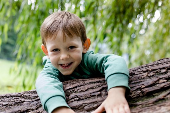 Ein lächelnder Junge spielt auf einem Baumstamm im Freien.