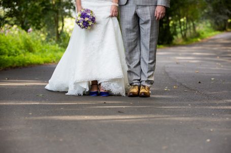 Hochzeitskleid und -anzug, Füße des Paares auf einem Weg, Braut hält einen Blumenstrauß.