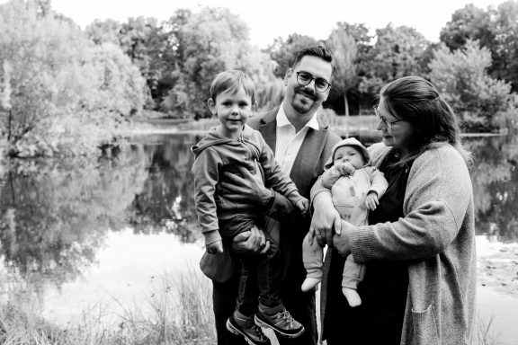 Eine Familie mit zwei Kindern vor einem See, umgeben von Bäumen.