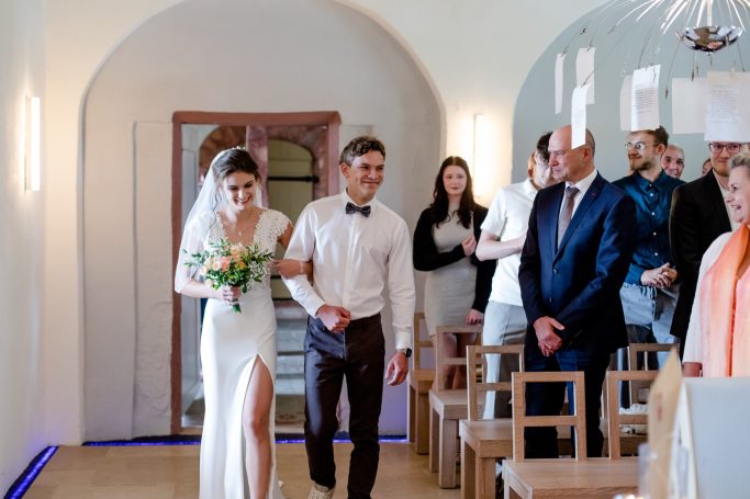 Brautpaar beim Eintritt in die Hochzeitszeremonie, umgeben von Gästen.