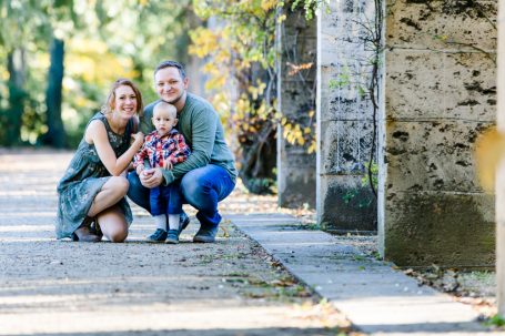 Familie posiert lächelnd im Freien, umgeben von Bäumen und Steinsäulen.