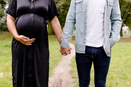 Schwangere Frau und Mann halten Händchen auf einem Weg in der Natur.