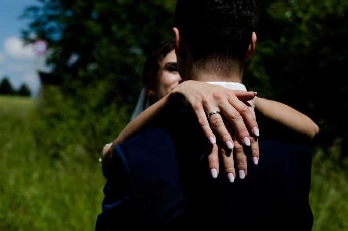 Ein Brautpaar umarmt sich, die Braut zeigt elegante Ringe an ihrer Hand.