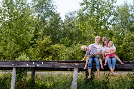 Zwei Frauen und zwei Kinder sitzen auf einem Holzsteg in einer grünen Landschaft.