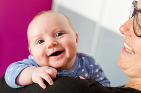 Lächelndes Baby, das auf dem Arm einer Person sitzt, mit fröhlichem Ausdruck.