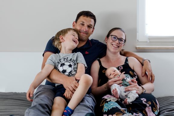 Familie sitzt zusammen auf einem Sofa, lächelnd mit zwei Kindern.