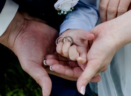 Hände von Erwachsenen halten die Hand eines Kindes, die Ringe sind sichtbar.