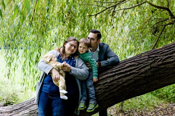 Familie posiert lachend im Freien, umarmt einander und hält ein Kuscheltier.