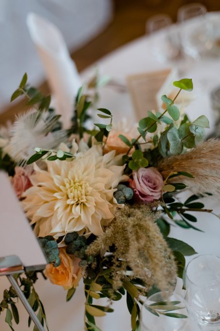 Blumenarrangement mit Dahlien, Rosen und grünem Blattwerk auf einem Tisch.
