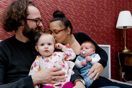 Eine Familie mit zwei kleinen Kindern sitzt zusammen. Eine Frau küsst das Baby.