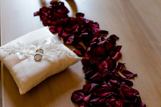 Rosenblätter liegen auf einem Tisch neben einem Ringkissen mit Ringen.