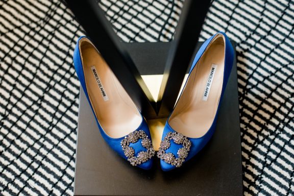 Blaue Pumps mit Schmuckdetails auf einem schwarz-weißen gemusterten Untergrund.