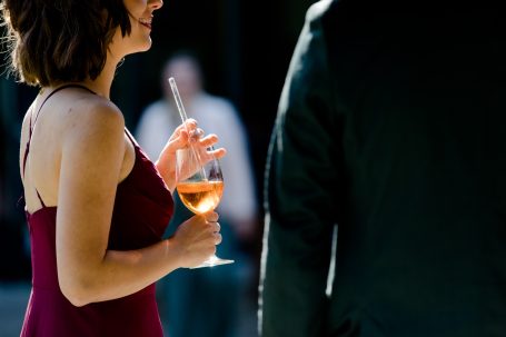 Frau in rotem Kleid hält ein Glas mit roséfarbenem Getränk, Blick von hinten.